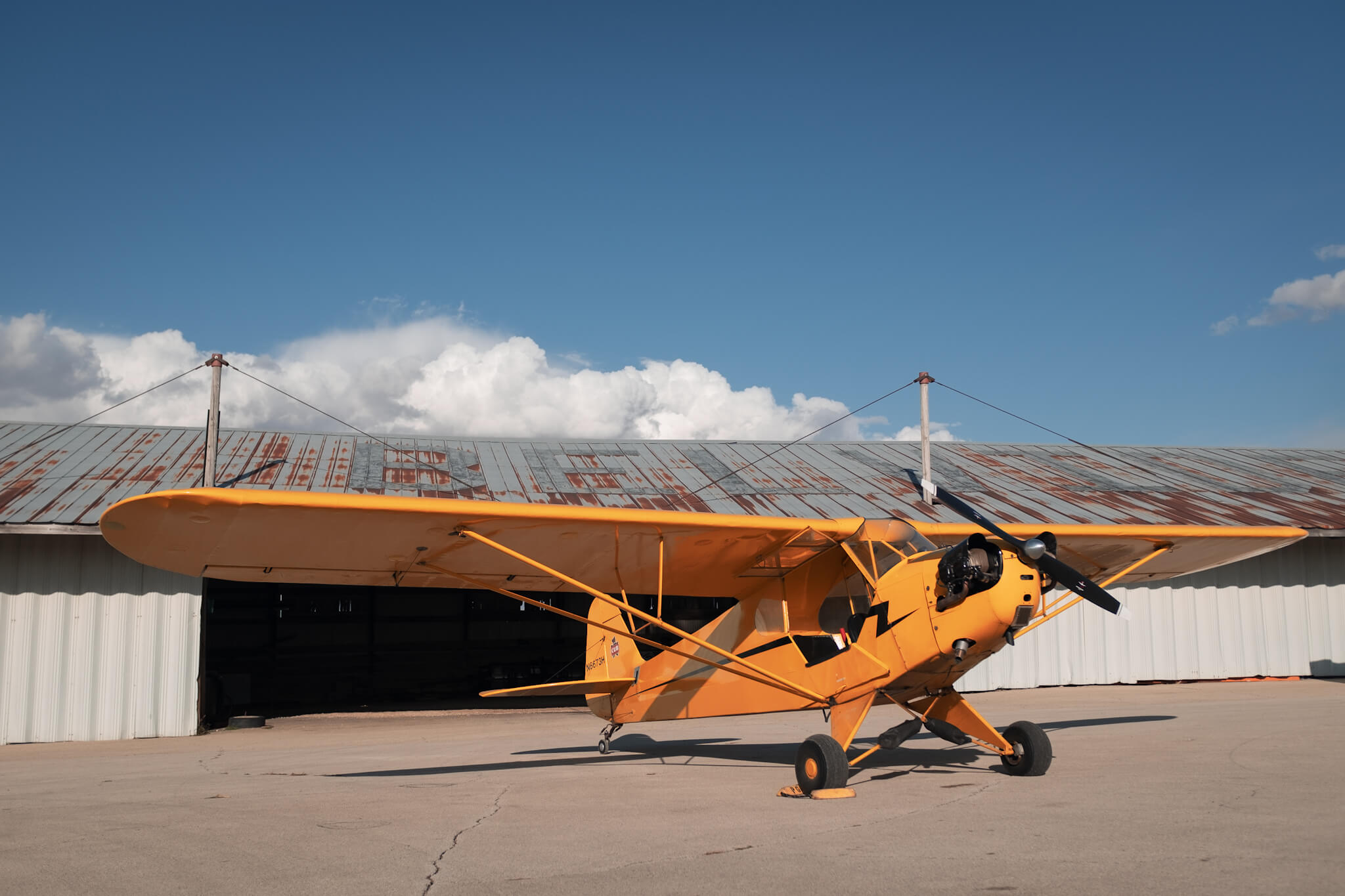 Yellow Piper J-3 Cub (N6673H) parked outside hangar at Poplar Grove Airport (C77) on sunny day